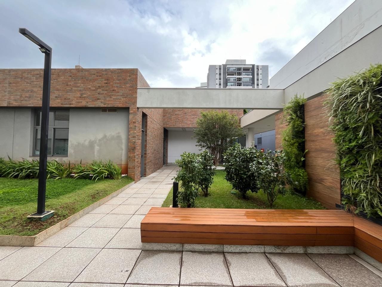 Área verde do Sartoria Taquaral com banco de madeira e pavimento em tijolo aparente