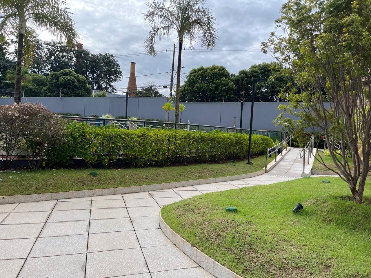 Jardim com gramado e arbustos ao lado da torre do Sartoria Taquaral