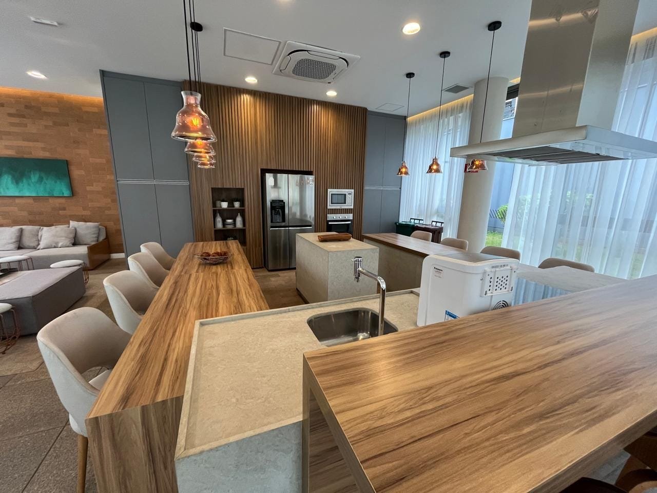 Área de jantar do espaço gourmet Sartoria Taquaral com mesa longa e pendentes cobre