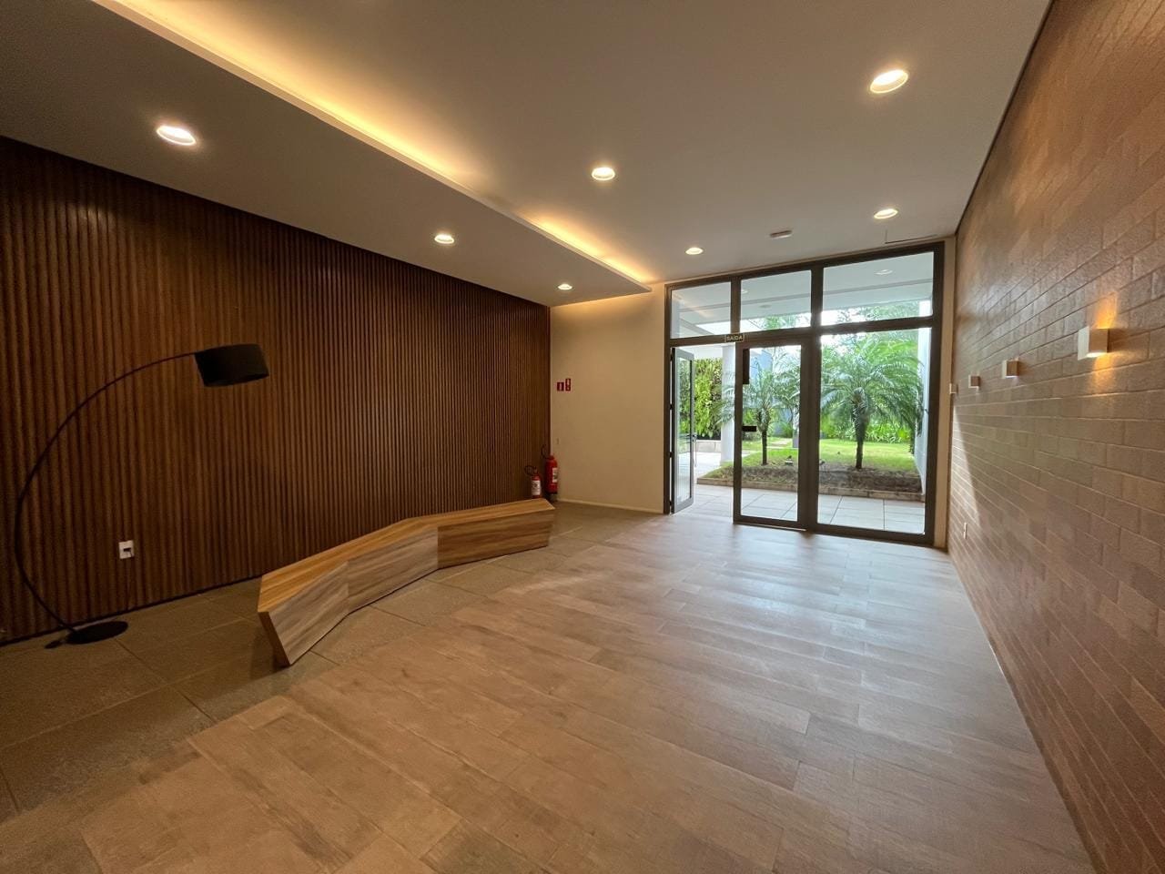 Hall interno do Sartoria Taquaral com parede ripada retroiluminada e banco curvo em madeira