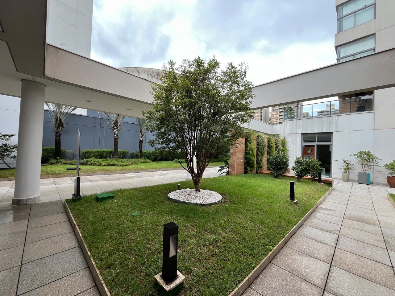 Jardim interno central do Sartoria Taquaral com árvore ornamental e bolards